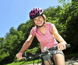 Portrait of a teenage girl on a bicycle in summer park outdoors